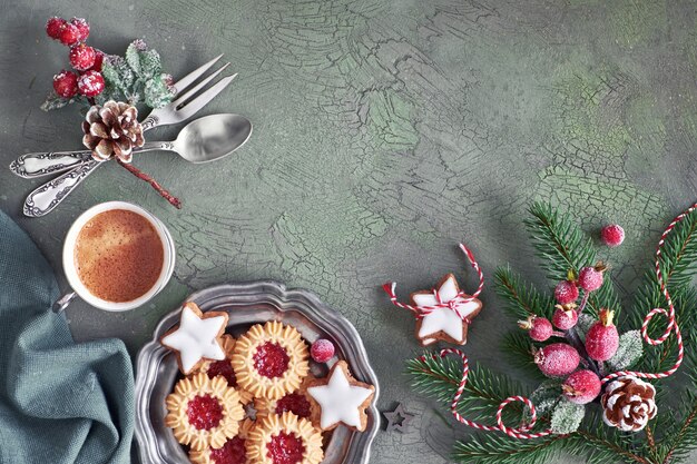 Piatto disteso con decorazioni natalizie in verde e rosso con bacche glassate e bigiotteria, caffè e biscotti di Natale