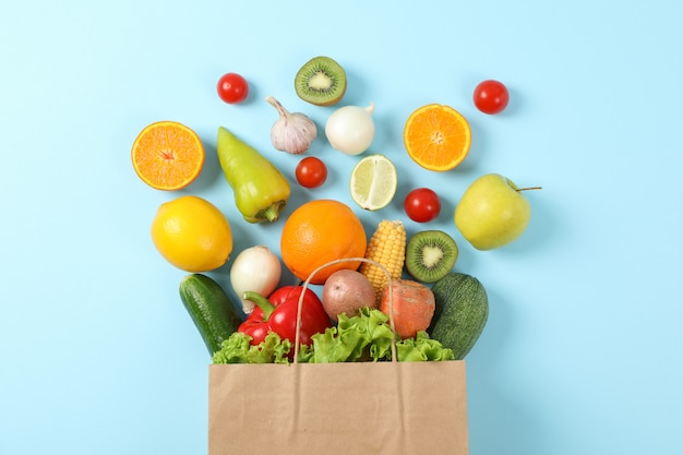 Piatto disteso con sacchetto di carta, frutta e verdura su blu