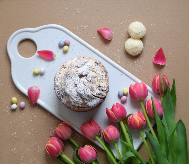 Piatto disteso con torta su tagliere in legno con tulipani, petali e caramelle