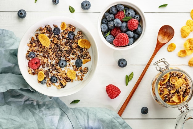 Piatto disteso con una colazione sana e leggera con cereali e bacche su un tavolo di legno bianco