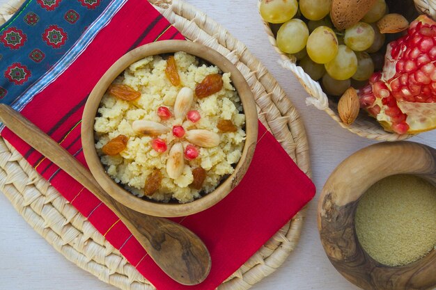 Piatto dolce tradizionale tunisino -Masfouf: cuscus zuccherato con uvetta e mandorle. Il cesto intrecciato è pieno di frutta. Sfondo. Vista dall'alto.