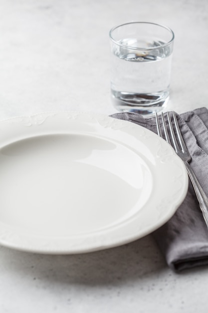 Piatto e bicchiere d&#39;acqua vuoti, fondo bianco. Concetto di digiuno medico.