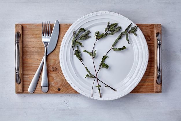 Piatto in ceramica bianca e foglie di menta secca e un vassoio con posate su un tavolo in legno dipinto di chiaro Mockup per la dimostrazione di un piatto Vista dall'alto Posa piatta