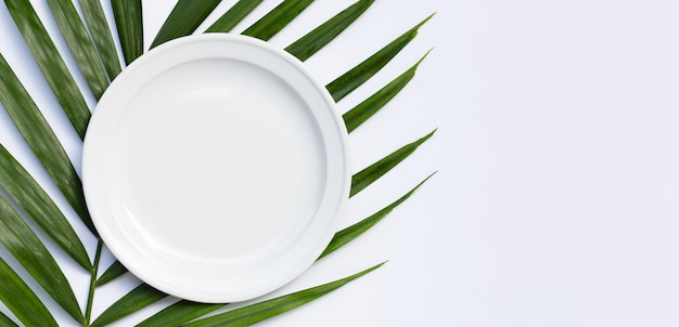 Piatto in ceramica bianco vuoto su foglie di palma tropicale su bianco