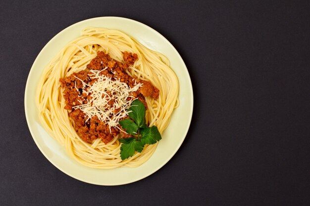 Piatto in porcellana con spaghetti e ragù alla bolognese su fondo nero. Vista dall'alto.