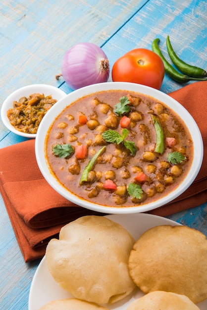 Piatto indiano piccante ceci curry noto anche come Chola o Chana Masala o comunemente Chole, servito servito con puri fritti o poveri su sfondo colorato o in legno. Messa a fuoco selettiva