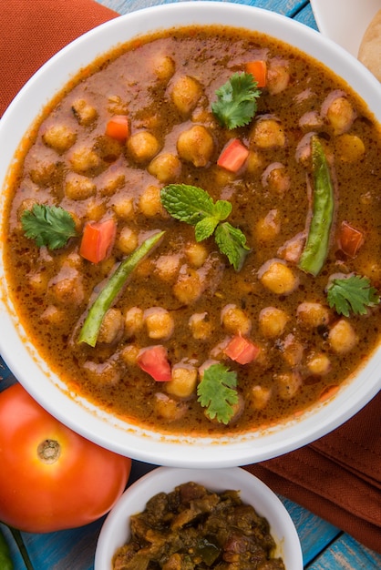 Piatto indiano piccante ceci curry noto anche come Chola o Chana Masala o comunemente Chole, servito servito con puri fritti o poveri su sfondo colorato o in legno. Messa a fuoco selettiva