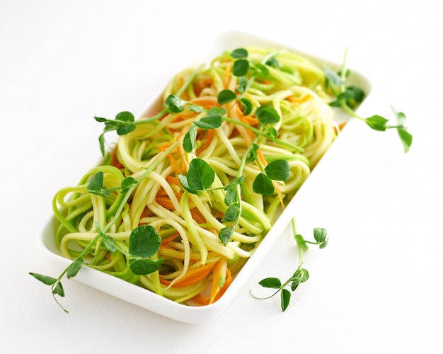 Piatto luminoso di zucchine giovani sotto forma di una pasta con piselli microgreen su uno sfondo bianco