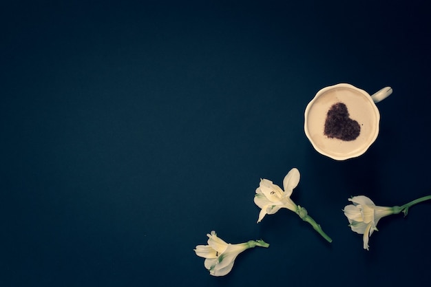 Piatto minimalista laici tre fiori e caffè con panna e cannella a forma di cuore in tazza su sfondo scuro