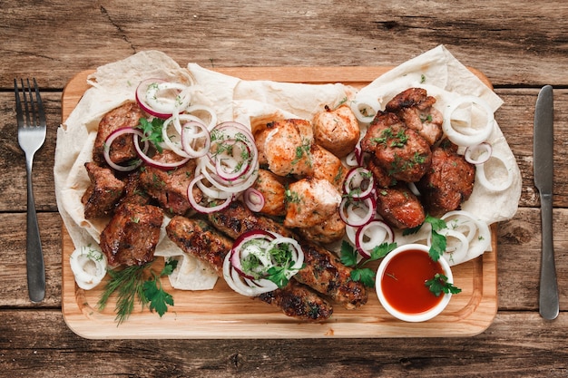 Piatto misto di carne alla griglia. Deliziosa carne alla griglia assortita servita su pane pitta con erbe aromatiche, cipolla e salsa di pomodoro, vista dall'alto.