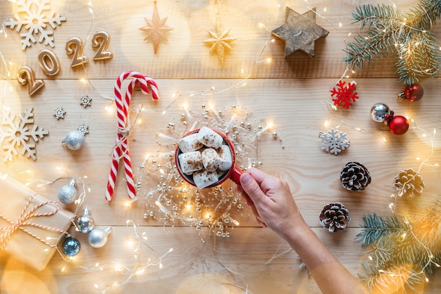 Piatto natalizio con una tazza di cioccolata calda marshmallow, bastoncini di zucchero, luci natalizie e numeri dorati del 2022