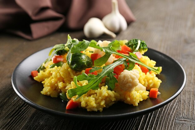 Piatto nero con risotto alle verdure sul tavolo di legno servito