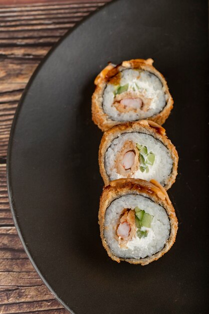 Piatto nero di rotoli di sushi collocato su un tavolo di legno.