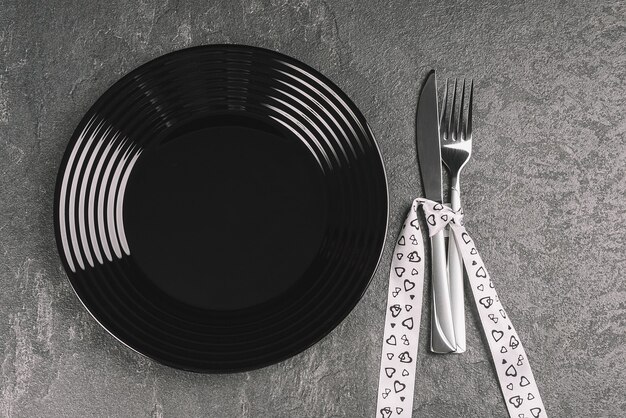 Piatto nero vuoto e argenteria sulla tavola di pietra nera decorata per il giorno di San Valentino