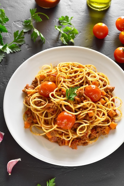 Piatto per la cena Spaghetti alla bolognese con carne macinata e pomodorini su tavola di pietra nera