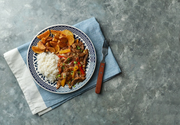 Piatto peruviano Lomo saltado, a base di filetto di manzo con cipolla rossa, peperoncino giallo, pomodori, con patate fritte e riso