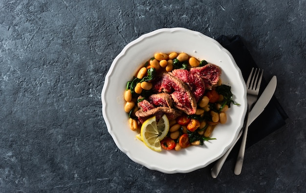 Piatto piano con bistecca di manzo con fagioli bianchi, spinaci e pomodori