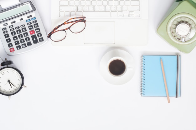 Piatto piano della scrivania di lavoro con il computer portatile bianco, la cancelleria e la tazza di caffè