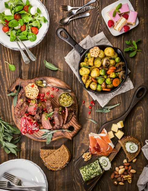 Piatto piatto di delizioso tavolo da pranzo con bistecca di carne arrosto, antipasti e dessert.