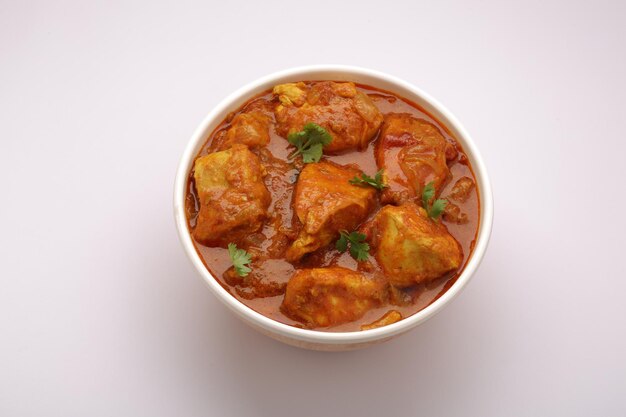 Piatto piccante indiano di pollo al curry guarnito con foglia di coriandolo e disposto in un contenitore di legno