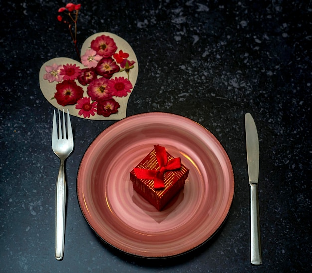 Piatto rosa vuoto con un regalo forchetta e coltello Cuore pieno di fiori rossi Concetto di San Valentino