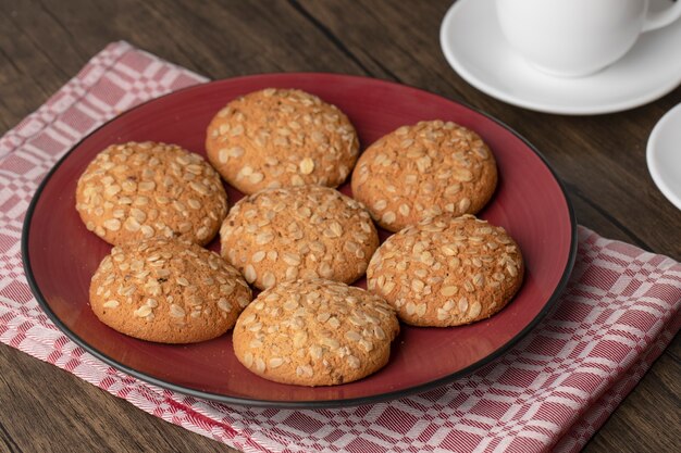 Piatto rosso con biscotti di farina d'avena e tazze di tè caldo sulla tavola di legno