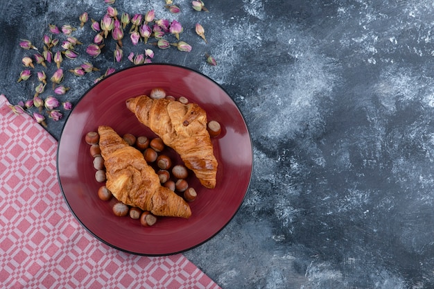 Piatto rosso di croissant dolci con nocciole sgusciate su marmo.