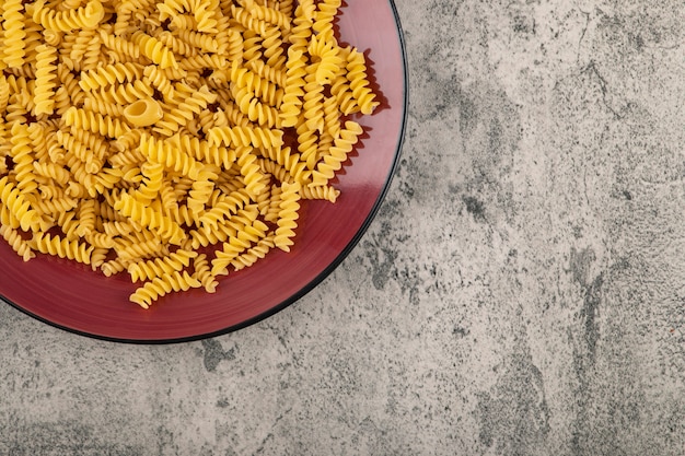 Piatto rosso di fusilli sani crudi sul tavolo di pietra.