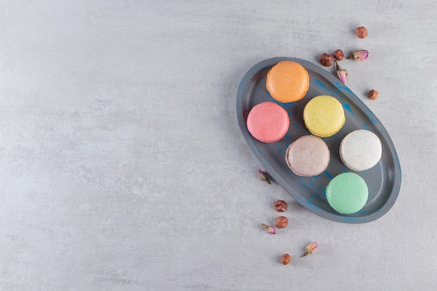 Piatto scuro di amaretti dolci colorati con rose sul tavolo di pietra.