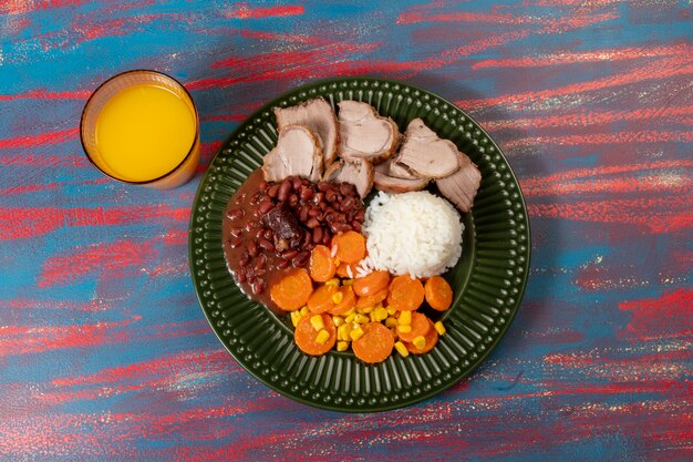 Piatto tipico brasiliano con riso, fagioli rossi, insalata di maiale e carote e mais brasato in un piatto verde