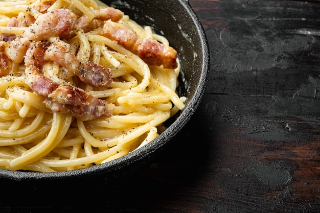 Piatto tradizionale italiano spaghetti alla carbonara con pancetta in salsa di panna, in padella in ghisa, sul vecchio tavolo in legno scuro, con spazio di copia