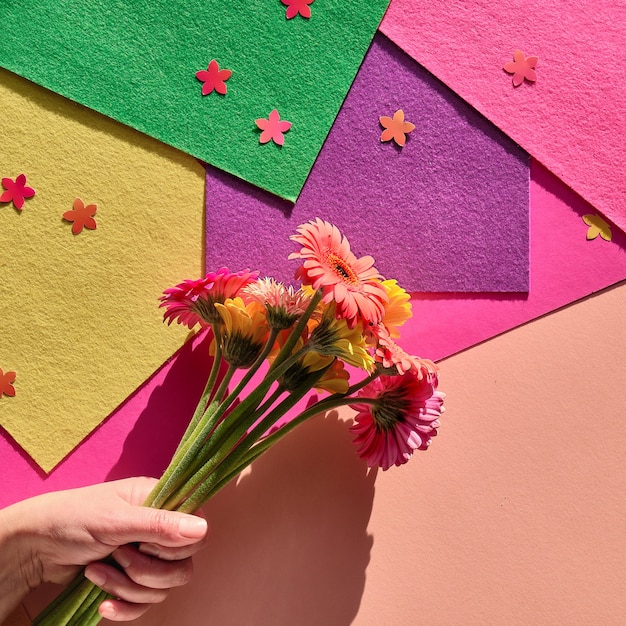 Piatto vibrante laici con la mano che tiene tre fiori di gerbera su carta geometrica