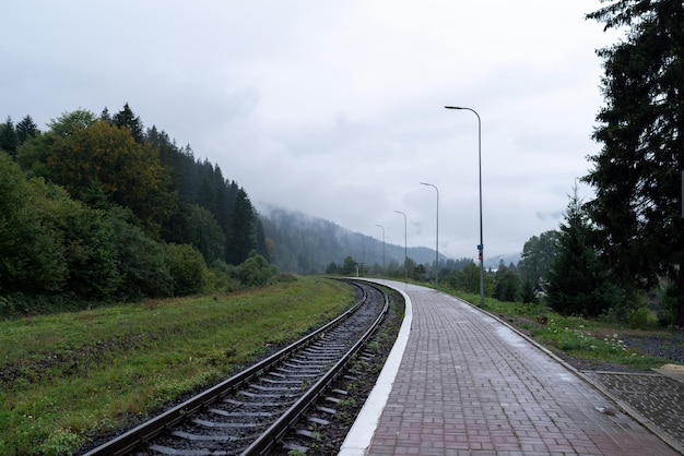 Piazza della stazione ferroviaria Ferrovia che porta alle montagne Tempo nuvoloso alla stazione Luci di strada sopra la piattaforma Tempo nuvolato e piovoso