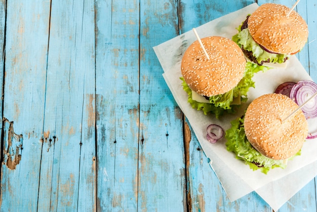 Pic-nic, Fast food. Cibo malsano. Hamburger saporiti freschi deliziosi con la cotoletta di manzo, le verdure fresche e il formaggio sulla vecchia tavola di legno blu rustica con soda dolce. vista dall'alto