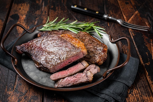 Picanha alla griglia o bistecca di manzo con controfiletto con rosmarino in vassoio in acciaio Sfondo in legno Vista dall'alto