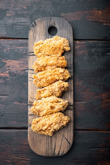 Piccanti tagli di ali di pollo impanate fritte sul tavolo di legno scuro, vista dall'alto.