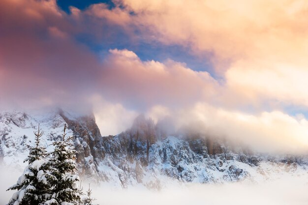 Picchi di montagna con nuvole al tramonto. Alpi dolomitiche invernali innevate. Val di Fassa, Italia. Bellissimo paesaggio invernale