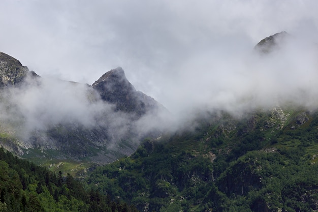 Picco della montagna con ghiacciai contro la superficie delle nuvole e del cielo