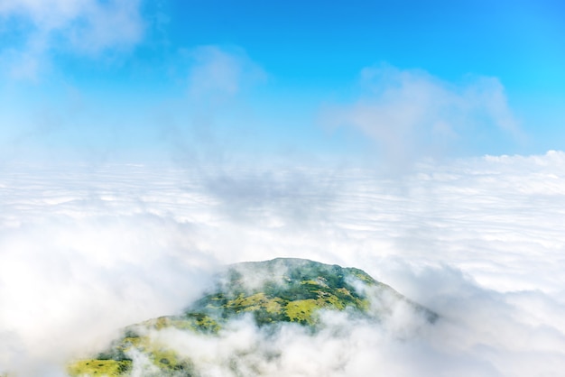 Picco di montagna verde in nuvole bianche e cielo blu