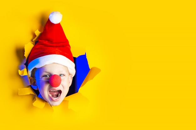 Piccola allegra Babbo Natale in cappello sorride, uscendo dallo sfondo giallo sfilacciato illuminato dalla luce al neon