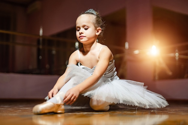 Piccola ballerina in tutù bianco seduta sul pavimento