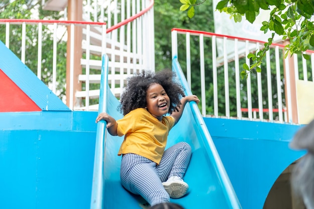 Piccola bambina africana felice che scivola e gioca nel parco all'aperto durante le vacanze estive I bambini dell'asilo si divertono e si divertono con le attività all'aria aperta imparando ed esercitando a scuola
