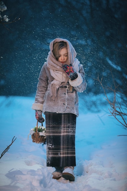 Piccola bambina con un cesto va e cerca i primi fiori sotto la neve nella foresta in