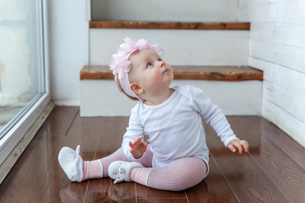 Piccola bambina strisciante di un anno che si trova sul pavimento in un soggiorno luminoso vicino alla finestra smili