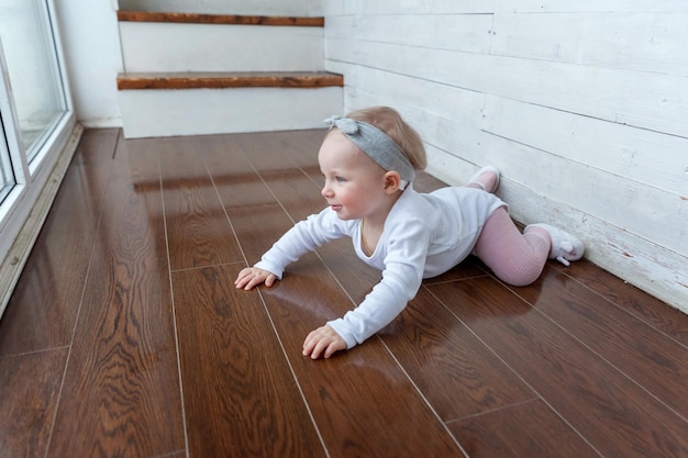 Piccola bambina strisciante di un anno che si trova sul pavimento in un soggiorno luminoso vicino alla finestra smili