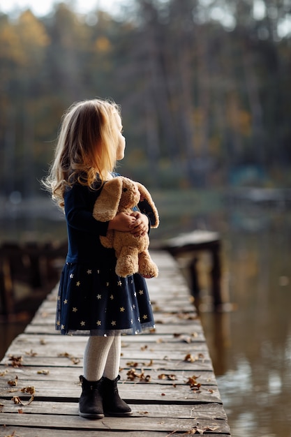 Piccola bella ragazza che tiene un giocattolo in sue mani nel parco di autunno vicino all'acqua.