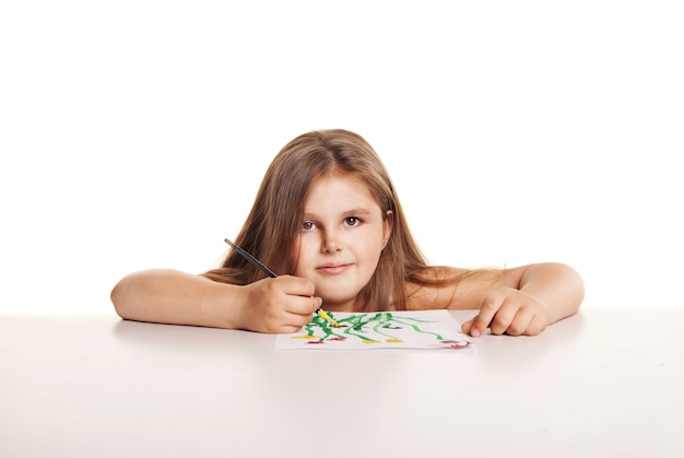 Piccola bella ragazza con pennello dipinge fiori su carta su sfondo bianco