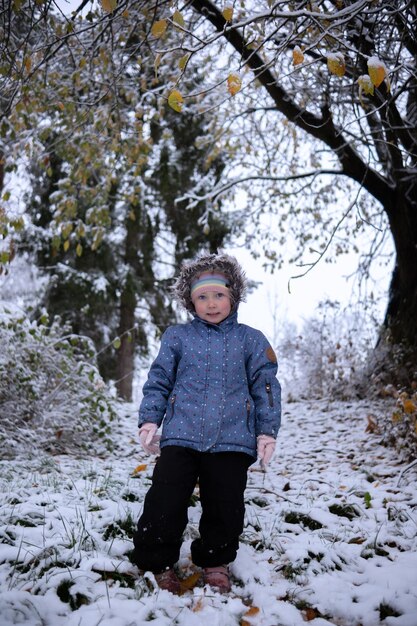 Piccola bella ragazza in abiti invernali in piedi da sola nel mezzo di una foresta innevata