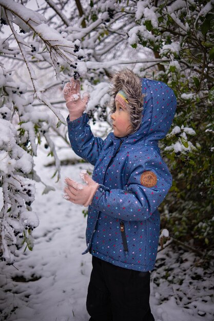 Piccola bella ragazza in abiti invernali in piedi da sola nel mezzo di una foresta innevata