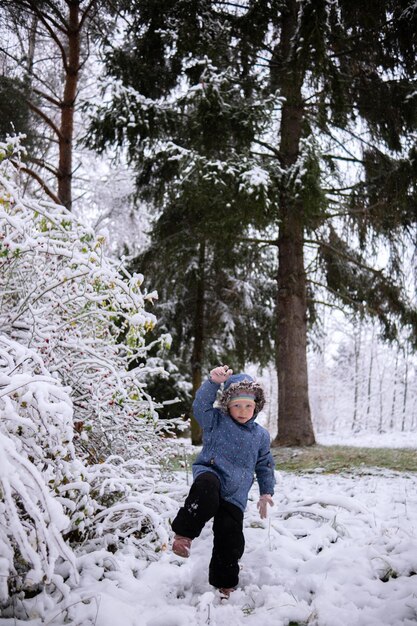 Piccola bella ragazza in abiti invernali in piedi da sola nel mezzo di una foresta innevata